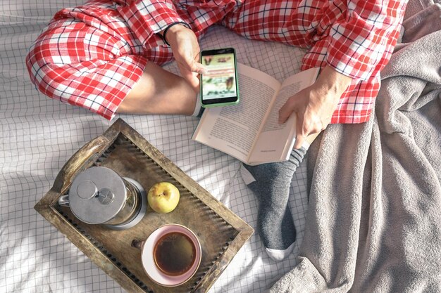 A close-up photo of a person holding a book and a smartphone, with a social media app open showing a book review. The background should be a cozy, well-lit home setting.
