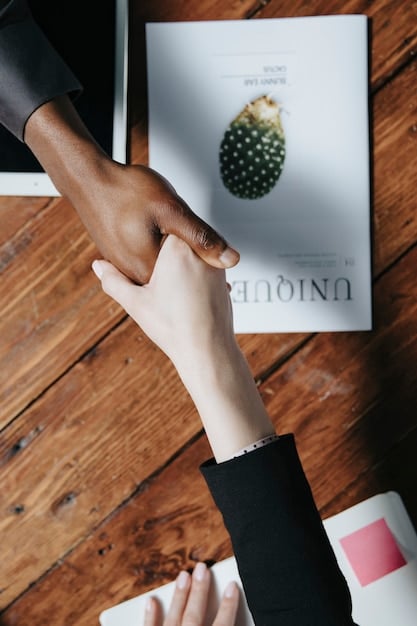 A close-up shot of two people shaking hands over a table with books. One person appears to be an author, and the other an event organizer. The setting is a bright and inviting conference room, emphasizing a professional and cooperative atmosphere.
