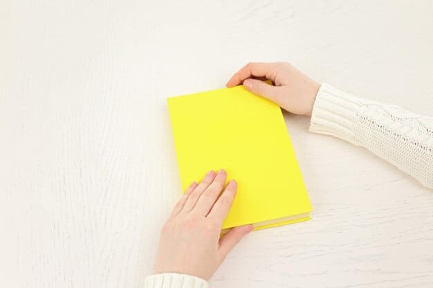 A close-up shot of hands holding an open physical book with sticky notes marking pages, while in the background, a laptop displays a book review platform with multiple positive reviews for the same book. This represents the blend of traditional reading and digital review engagement.