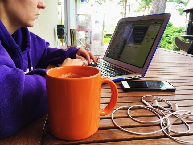 A person typing on a laptop, surrounded by books and a coffee cup, illustrating the process of building an author platform online.