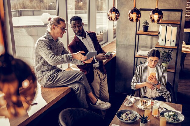 A diverse group of people sitting in a cozy, modern cafe, each absorbed in reading a book or tablet. Some are subtly taking notes, suggesting active engagement and critical thinking. The atmosphere is warm and inviting.