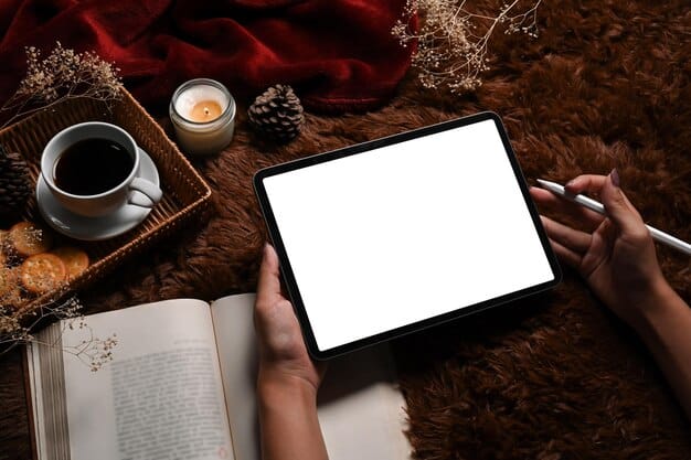 A person holding a tablet showing an author interview or a literary podcast, with open books and a 'currently reading' bookmark on a cozy, well-lit desk.