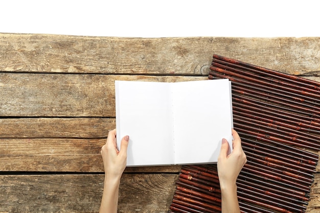 A person's hands holding an open book, with the focus on the pages. The background is blurred, suggesting a cozy, natural light setting indoors, emphasizing the act of reading and engaging with a story.